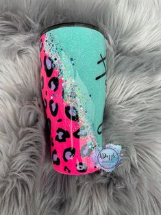 a pink and blue leopard print cup with glitter on the bottom sitting on a furry surface