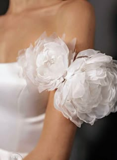 a woman in a white dress with two large flowers on her arm and the other hand