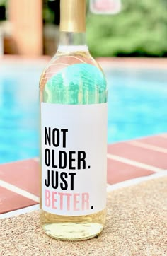 a bottle of wine sitting on top of a table next to a swimming pool with the words not older just better