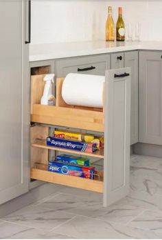 an open cabinet in the middle of a kitchen with white counter tops and gray cabinets