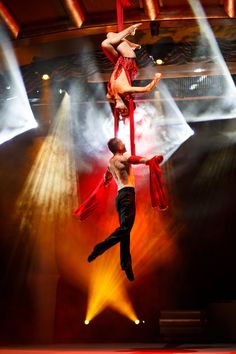 two circus performers performing aerial acrobatic tricks in front of bright lights on stage