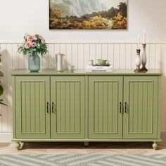 a green sideboard with two vases and flowers on it next to a painting