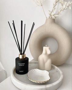 a white vase sitting on top of a table next to a black and white candle