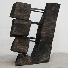 a sculpture made out of wood sitting on top of a cement floor next to a white wall