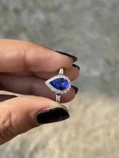 a woman's hand holding an engagement ring with a pear shaped blue sapphire surrounded by diamonds