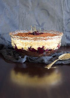 a dessert dish with cherries in it on a table next to a silver spoon