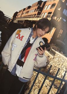 a young man standing in front of a building holding a cell phone and looking at it