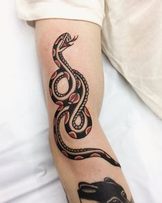 a black and red snake tattoo on the left arm with an animal in it's center