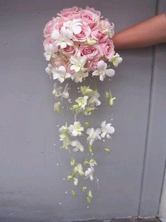 a person holding a bouquet of pink and white flowers in their hand on the side of a building