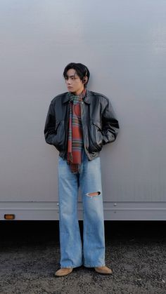 a man standing in front of a wall with his hands on his hips wearing jeans and a leather jacket