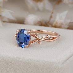 a blue stone ring sitting on top of a white box with flowers in the background