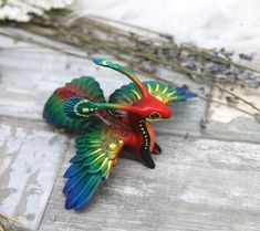 a colorful bird figurine sitting on top of a wooden table next to dried flowers