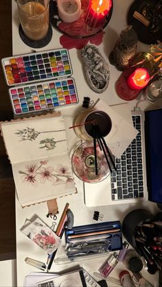 the desk is cluttered with art supplies and candles