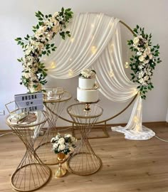 a table topped with two cakes covered in white flowers and greenery next to a gold stand