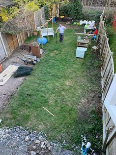 a man standing in the back yard next to a fence and lawn with various items on it