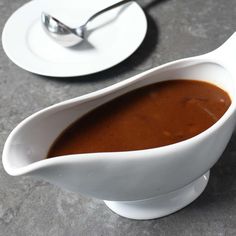 a white gravy dish with sauce in it on a table next to a fork and spoon