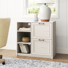 a white cabinet with two drawers next to a chair and lamp on top of it