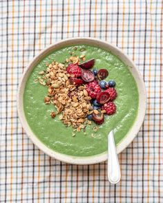 a bowl filled with green smoothie topped with berries and granola next to a spoon