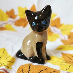 a black and white cat figurine sitting on a tablecloth with yellow leaves