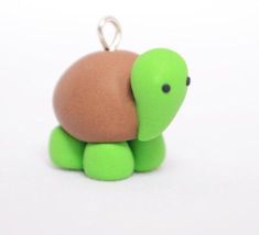 a green and brown turtle keychain sitting on top of a white table next to a black object