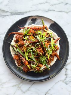 a black plate topped with meat and veggies on top of a marble table