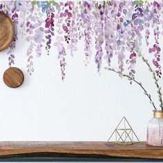 purple flowers are hanging on the wall next to a vase