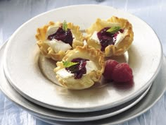 three small pastries on a plate with raspberries