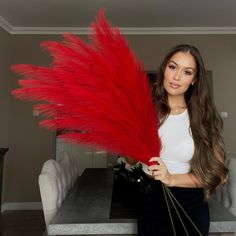 a woman holding a red feathered plant in front of a table with flowers on it