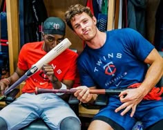 two baseball players sitting next to each other in the dugout, one holding a bat