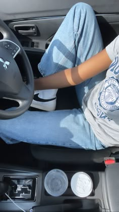 a person sitting in the driver's seat of a car with their feet on the steering wheel