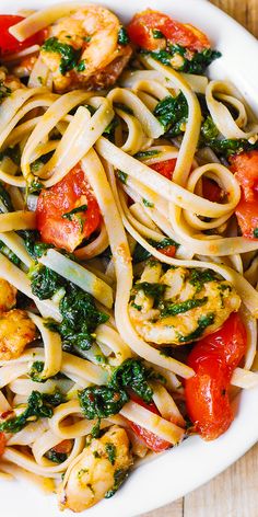 pasta with shrimp, tomatoes and spinach in a white bowl on a wooden table