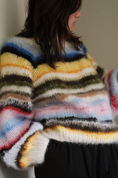 a woman wearing a multicolored striped sweater and black pants standing in front of a white wall