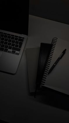 a laptop computer sitting on top of a desk next to a notebook