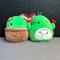 two green stuffed animals sitting next to each other on a gray surface with a black wall behind them