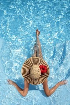 a woman wearing a straw hat floating in a pool with her feet up on the water