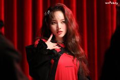 a woman in red and black dress standing next to a red curtain with her finger up