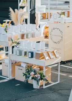 an outdoor market with flowers, candles and other items on the table for sale in front of it