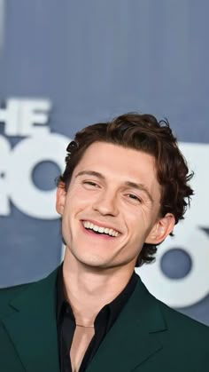 a man in a green suit smiles at the camera while wearing a black shirt and tie