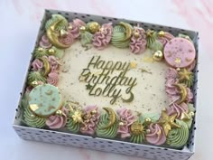 a birthday cake in a box decorated with pink, green and gold icing that says happy birthday