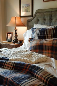 an unmade bed with plaid sheets and blankets on it, next to a lamp