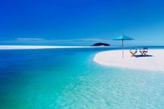 two chairs and an umbrella are on the shore of a beach with clear blue water