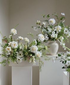 two white vases with flowers in them sitting on a shelf next to each other