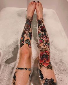 a person with tattoos on their legs sitting in a bathtub