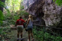 two people are walking up a path in the woods near a rock formation and trees