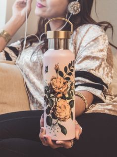 a woman sitting on a couch holding a water bottle with flowers painted on the side