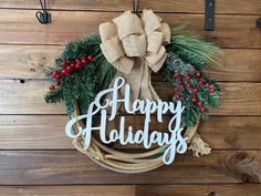 a christmas wreath with the words happy holidays hanging on a wooden wall next to hooks