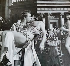 an old black and white photo of two women kissing in front of a crowd with men dressed as roman soldiers