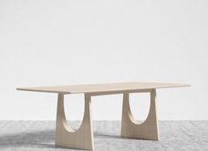 a wooden table with two curved legs on the top and bottom, in front of a white wall