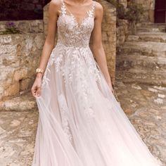 a woman in a wedding dress standing on the side of a stone building with her hands in her pockets