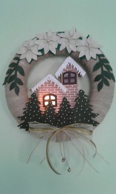 a wreath with a house and trees on it is hanging from the side of a wall